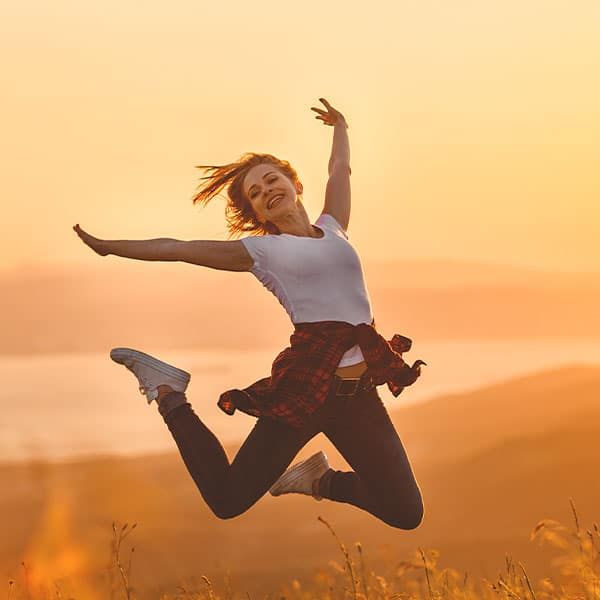 Eine Frau springt im Feld bei Sonnenuntergang voller Energie und Lebensfreude in die Luft.