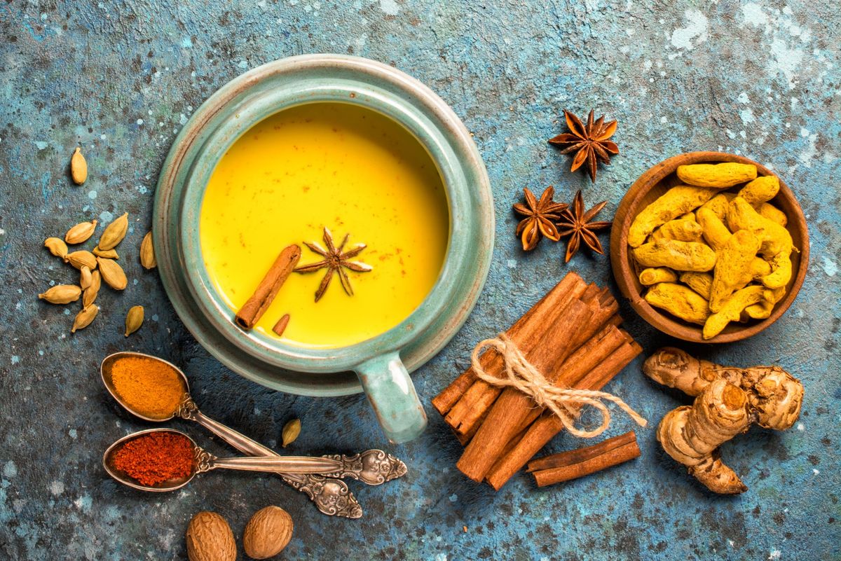 Top view of golden turmeric milk in big cozy cup for healthy life on blue concrete background with copy space