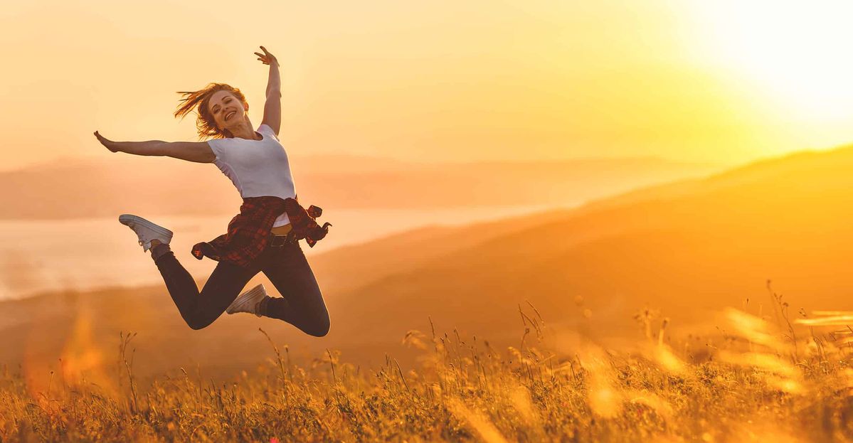 Eine Frau springt im Feld bei Sonnenuntergang voller Energie und Lebensfreude in die Luft.