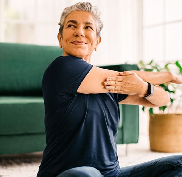 Eine Frau streckt sich zu Hause, um sich fit und vital, voller Energie zu fühlen.